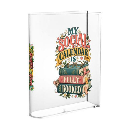 A clear acrylic desk calendar with a colorful graphic design on the front that reads 'MY SOCIAL CALENDAR IS FULLY BOOKED' with illustrated books, flowers, and a small bear. The calendar is shown open against a plain white background.