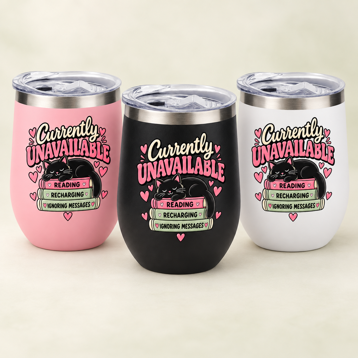 Three insulated stemless tumblers with clear lids are shown on a light beige background. The tumblers are pink, black, and white, each printed with a humorous message: 'Currently UNAVAILABLE' in pink and black script, with a black cat illustration, hearts, and a small sign that reads 'READING / RECHARGING / WONDING MESSAGES'.