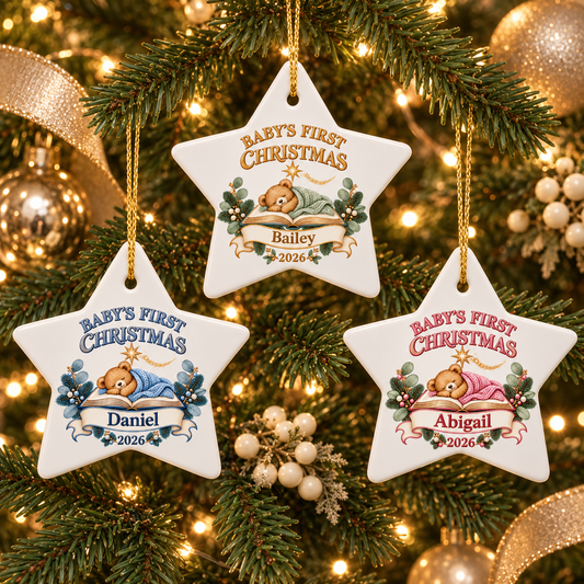 Three personalized white star Christmas ornaments hanging on a lit Christmas tree. Each ornament features a teddy bear illustration, holly leaves, and the text 'BABY'S FIRST CHRISTMAS' with a name and year below.