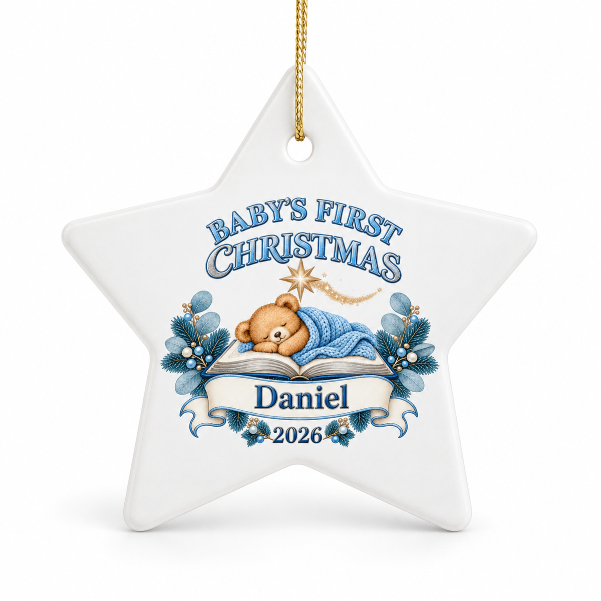 A white star-shaped ceramic Christmas ornament hanging by a gold string, featuring a personalized design for 'Baby's First Christmas' with a teddy bear sleeping under a blue blanket, blue holly leaves, and the name 'Daniel' with '2026'.
