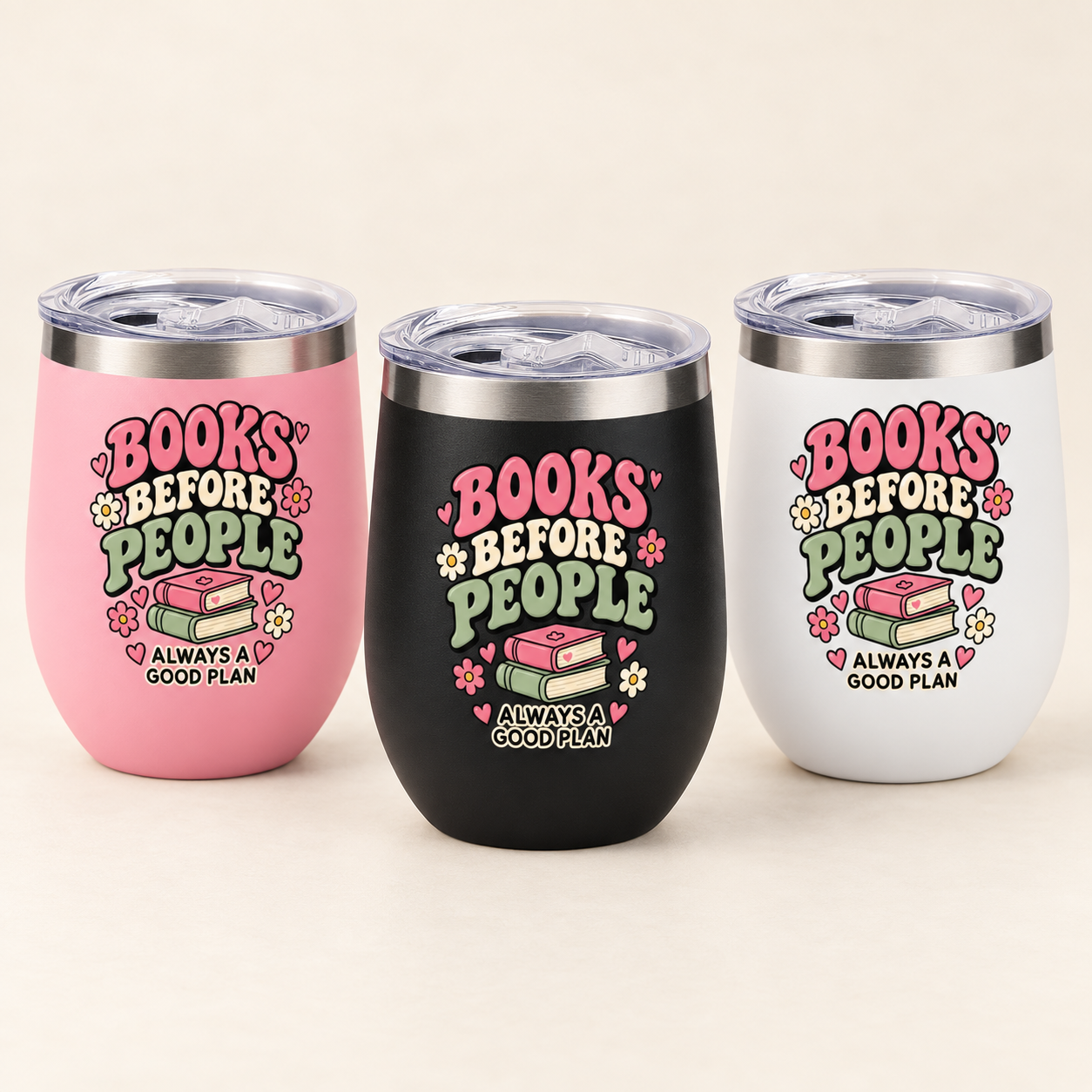 Three insulated stemless tumbler cups with clear lids are shown on a light beige background. The left cup is pink, the center cup is black, and the right cup is white, each printed with the phrase “BOOKS BEFORE PEOPLE ALWAYS A GOOD PLAN” and a small book-and-flower graphic.