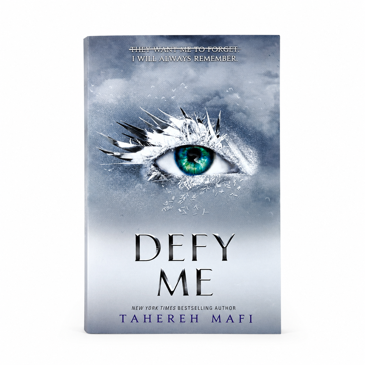 The book cover of 'Defy Me' by Tahereh Mafi, featuring a dramatic icy eye with a vibrant green iris on a gray, snowy background. The title is written in large, metallic silver letters, and the author's name is printed at the bottom.