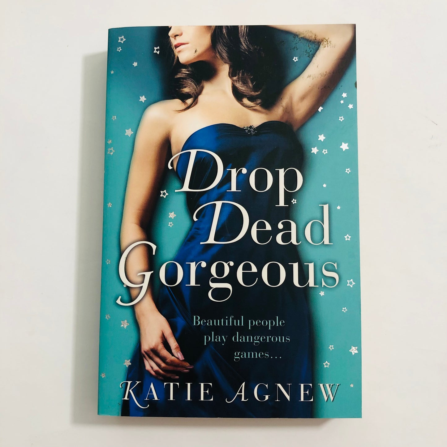 Book cover of 'Drop Dead Gorgeous' by Katie Agnew with a woman in a blue dress on a teal background.