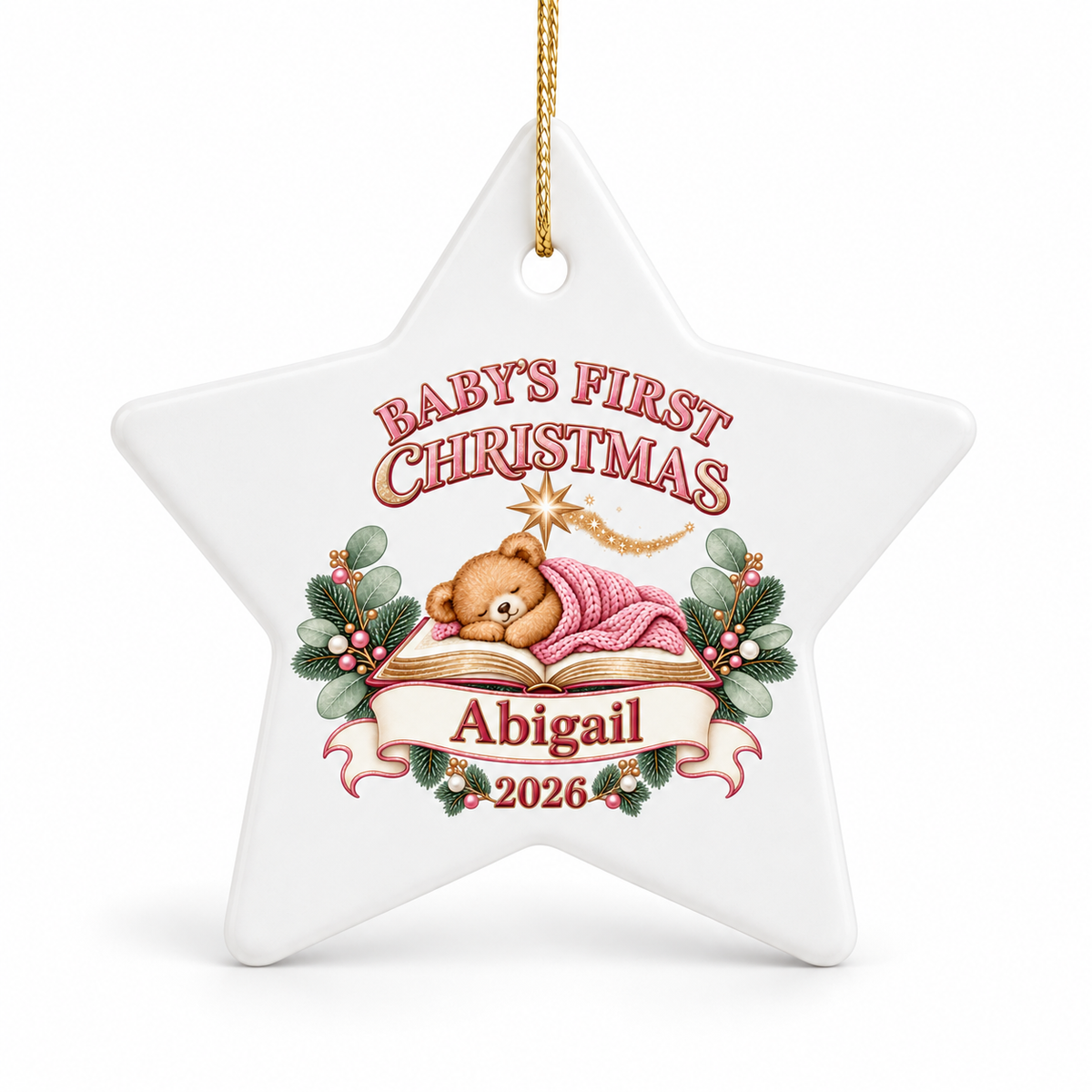 A white star-shaped ceramic Christmas ornament with a hanging loop, featuring a personalized design for 'Baby's First Christmas' with a teddy bear, pink blanket, holly leaves, and the name 'Abigail' with the year '2026'.