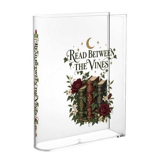 A clear acrylic book stand displaying a book cover with the title 'Read Between the Vines' and an illustration of vintage books, roses, and a crescent moon.