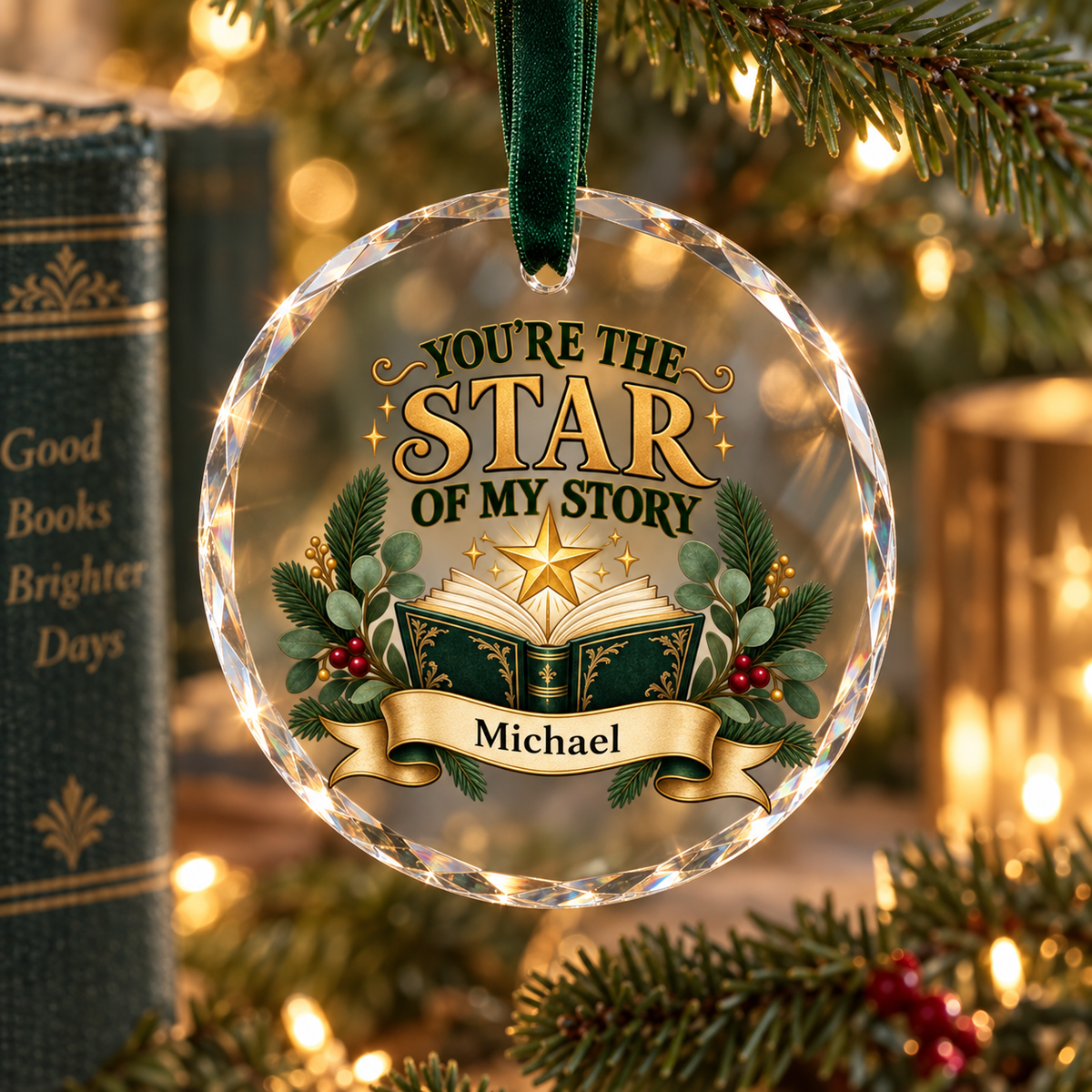 A round clear glass Christmas ornament hanging from a dark green ribbon, printed with the phrase “YOU’RE THE STAR OF MY STORY” above an open book, greenery, berries, and a personalized name banner reading “Michael.” The ornament is photographed on a blurred Christmas tree with warm lights and books in the background.